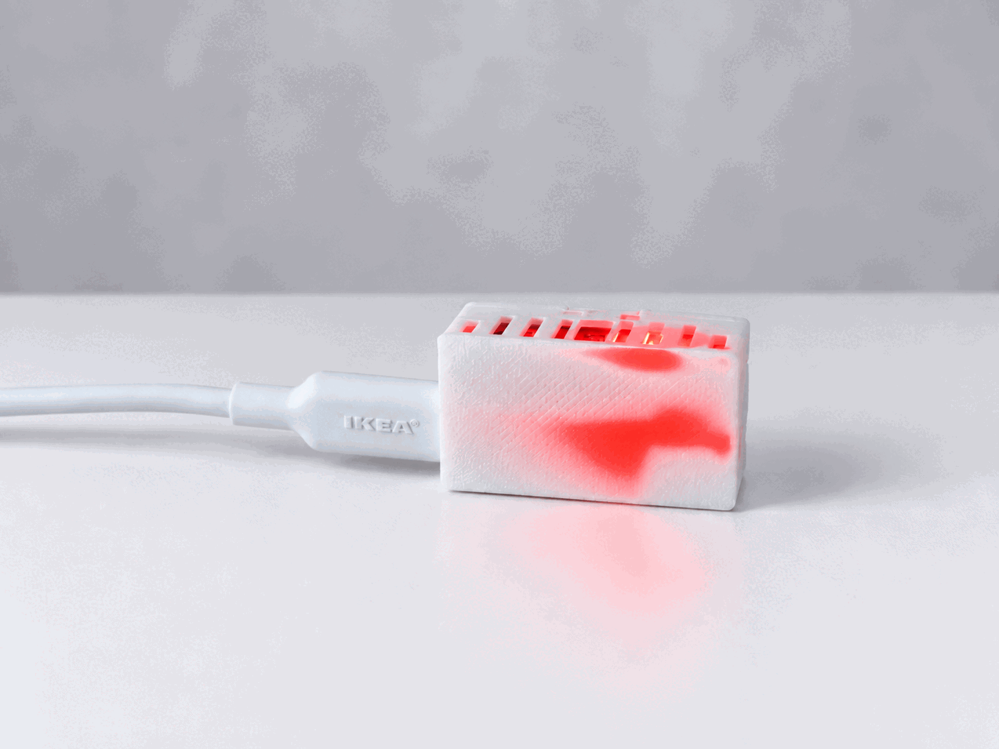 A USB-powered air quality monitor glowing red through its white enclosure and reflecting onto the tabletop.